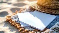 Summer vacation planning concept with blank postcards, straw hat and beach towel on sandy shore with warm sunlight creating peaceful holiday atmosphere.