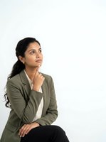 Thoughtful young woman of South Asian descent wearing olive blazer and white shirt, hand to chin in contemplative pose against white background, suitable for business and corporate concepts.