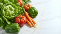 Fresh organic vegetables including lettuce, tomatoes, carrots, bell peppers and cucumbers arranged on white wooden background for healthy cooking and nutrition.