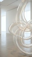 Contemporary glass sculpture with flowing curved tubes in minimalist gallery space with natural light from windows and polished concrete floor.