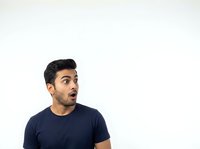 Young man with dark hair and olive complexion wearing navy blue t-shirt, displaying surprised or shocked facial expression, isolated on white background for portrait and commercial use.