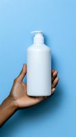 Hand holding white pump bottle with lotion, gel, or cleanser against blue background. Person with medium skin tone displaying cosmetic product for skincare, hygiene, or wellness branding.