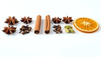 Aromatic spices and dried orange slice arranged on white background for cooking, baking and culinary projects.