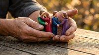 Elderly hands gently holding colorful wooden family figures representing unity, care and protection in warm outdoor setting with golden bokeh background.