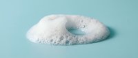 White foam bubble with delicate texture on soft blue background for skincare and beauty product advertising campaigns.