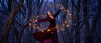 Young woman in burgundy dress dancing with glowing fairy lights in mystical forest at twilight creating magical atmosphere for fantasy storytelling.
