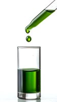Green liquid dropping from glass pipette into transparent shot glass on white background, capturing moment of falling drop in scientific or cocktail setting.