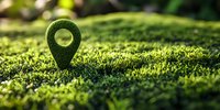 Green location pin marker covered in moss on natural grass background with soft bokeh effect, representing eco-friendly navigation and sustainable tourism concept.