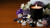Spa wellness scene with burning candle, healing crystals, gemstones and flowers on wooden surface for relaxation and meditation therapy.