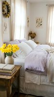 Cozy spring bedroom with lavender linen bedding, yellow daffodils in a vase, botanical prints, and sheer curtains in soft natural light.