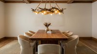 Modern dining room interior with wooden table, beige chairs and rustic chandelier. Contemporary home design with exposed ceiling beams and hardwood floors.