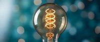 Vintage Edison light bulb with glowing spiral filament against blue bokeh background. Retro illumination concept for creative projects and design work.