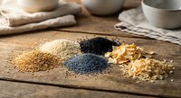 Assorted superfood seeds and grains including quinoa, chia, poppy seeds and oats arranged on rustic wooden cutting board for healthy cooking and nutrition.