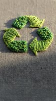 Green embroidered recycling symbol on natural burlap fabric representing eco-friendly sustainability and environmental awareness for Earth Day campaigns.