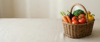 Wicker basket filled with fresh colorful vegetables on a linen tablecloth, featuring tomatoes, broccoli, carrots, and peppers.