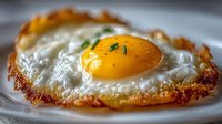 Close-up of sunny side up egg with crispy edges and bright yellow yolk garnished with fresh chives on white plate, perfect for breakfast menu photography.