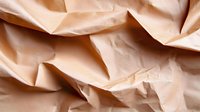 Crumpled peach-colored paper creating abstract geometric shapes and shadows with soft folds and textures, suitable for minimalist design backgrounds and creative layouts.