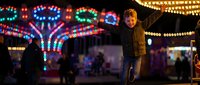 Young boy enjoying colorful carnival lights and festive atmosphere at night amusement park with bright illuminated rides creating magical entertainment experience.