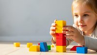 Young blonde girl playing with colorful wooden building blocks, stacking toys for early childhood development and creative learning activities.