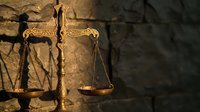 Golden scales of justice with ornate details against textured stone wall background symbolizing law, legal system, courthouse and judicial balance.