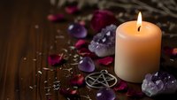 Mystical altar setup with burning candle, amethyst crystals, pentagram symbol and rose petals on wooden surface for spiritual rituals and meditation practices.