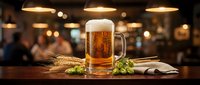 Fresh golden beer mug with foam on wooden bar counter with hops and wheat, warm pub atmosphere with blurred restaurant background for beverage advertising.
