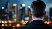 Professional businessman in dark suit gazing at illuminated city skyline at dusk, corporate success and urban ambition concept for business presentations.