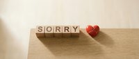 Wooden letter cubes spelling SORRY beside a broken red heart on a warm wood surface, conveying apology, regret, and emotional healing concepts.