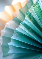 Delicate turquoise paper fan with intricate geometric pattern creates elegant pleated texture, soft focus background adds depth and artistic appeal for decorative designs.