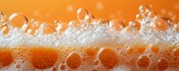 Macro shot of fizzy orange soda bubbles rising in carbonated drink against bright orange background, showing refreshing effervescent foam and liquid motion.