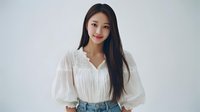 Young Asian woman with long dark hair wearing white blouse with embroidery details against minimal light background, smiling gently at camera.