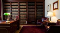 Elegant law office interior with wooden bookshelves filled with legal books, leather chairs, banker's lamp and warm lighting creating professional atmosphere.