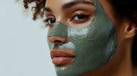 Young woman with green clay facial mask treatment, close up beauty portrait showing glowing skin and natural makeup for spa and skincare concept.