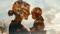 Double exposure silhouette of mother and child combined with autumn forest trees against dramatic sunset sky, showing family bond and nature connection.