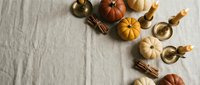 Autumn harvest flat lay with mini pumpkins, cinnamon sticks and brass candles on neutral linen background for seasonal home decor and thanksgiving styling.
