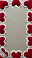Red velvet hearts with white lace trim arranged in decorative border frame on beige linen fabric background for romantic Valentine's Day crafts and love themes.