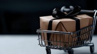Elegant brown gift box with black ribbon bow placed in miniature shopping cart against dark background, perfect for online shopping and retail concepts.