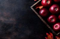 Fresh red apples in rustic wooden box on dark textured background with autumn maple leaves, copy space for seasonal fall harvest design.