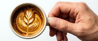 Barista holding ceramic cup with latte art leaf design, overhead view of hot coffee beverage for cafe, restaurant, or coffee shop marketing.