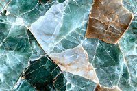 Natural marble stone surface in emerald green and copper tones showing intricate crack patterns and mineral veining, creating abstract geometric shapes.