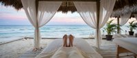 Couple relaxing on bed under beachfront pavilion with ocean view at sunset, tropical vacation getaway destination for honeymoon or romantic travel.