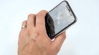 Hand holding smartphone with cracked screen display, isolated on white background. Broken mobile phone glass damage for repair service, insurance claim, or technology accident concept.