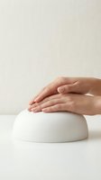 Female hands gently touching white ceramic dome shape on neutral background for skincare beauty wellness spa cosmetics product presentation.