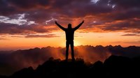 Male hiker silhouette celebrating success on mountain peak at dramatic sunset with arms raised against colorful sky and mountain ranges.