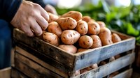 Fresh harvested potatoes in rustic wooden crate at farmers market, male hand selecting organic produce, natural food shopping concept with blurred background.