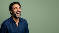 Middle-aged man with dark beard and hair wearing navy blue shirt, laughing with genuine expression against soft green background, suitable for business, lifestyle, and portrait projects.