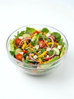 Fresh mixed green salad with tomatoes, bell peppers, and vegetables in a glass bowl, isolated on white background for food and nutrition content.