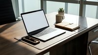 Laptop with blank white screen on wooden desk with notebook, coffee mug, and plant in bright modern office workspace.