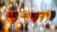 Row of wine glasses filled with different varieties from white to rose and red against blurred golden bokeh lights creating romantic ambiance for wine tasting event.
