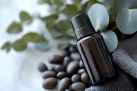 Dark glass essential oil bottle with massage stones and eucalyptus leaves on gray background, wellness and aromatherapy spa composition for natural cosmetics.